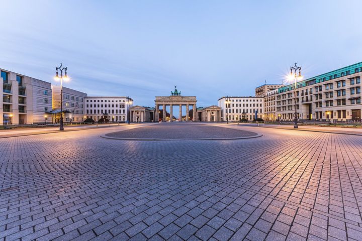 The empty cobbled Pariser Platz at dusk, with the Brandenburg Gate at the far end and the street lamps lit.